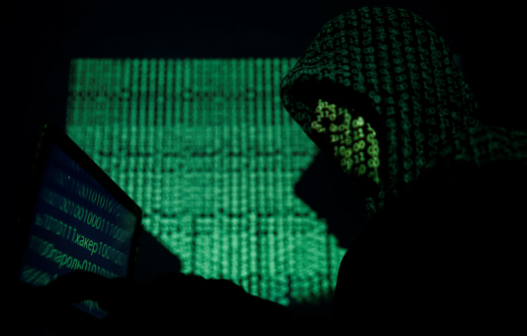 FILE PHOTO: A hooded man holds a laptop computer as cyber code is projected on him in this illustration picture taken on May 13, 2017. REUTERS/Kacper Pempel/Illustration